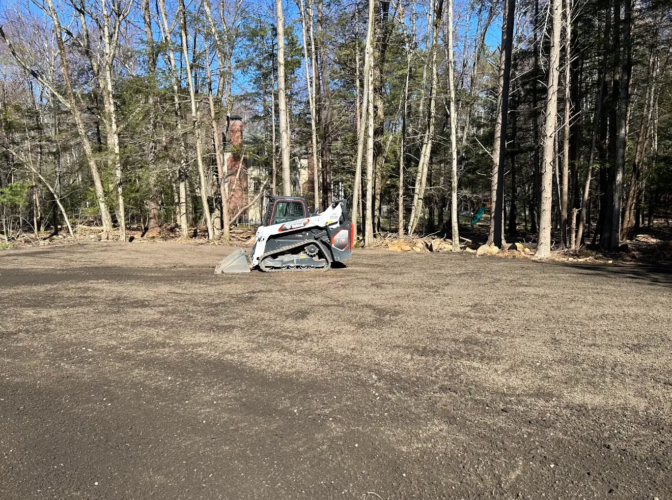 Freshly cleared and graded yard with a skid steer near the tree line